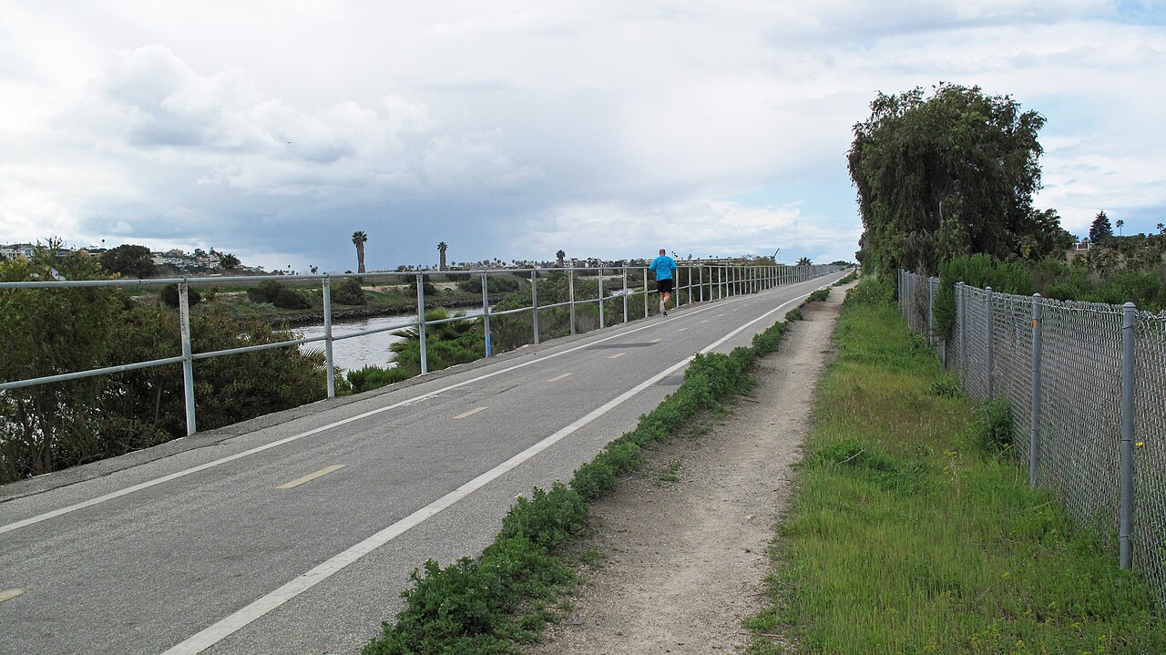 A marked paved Ballona Creek bikeway with walkers and Marina del Rey buildings in the distance
